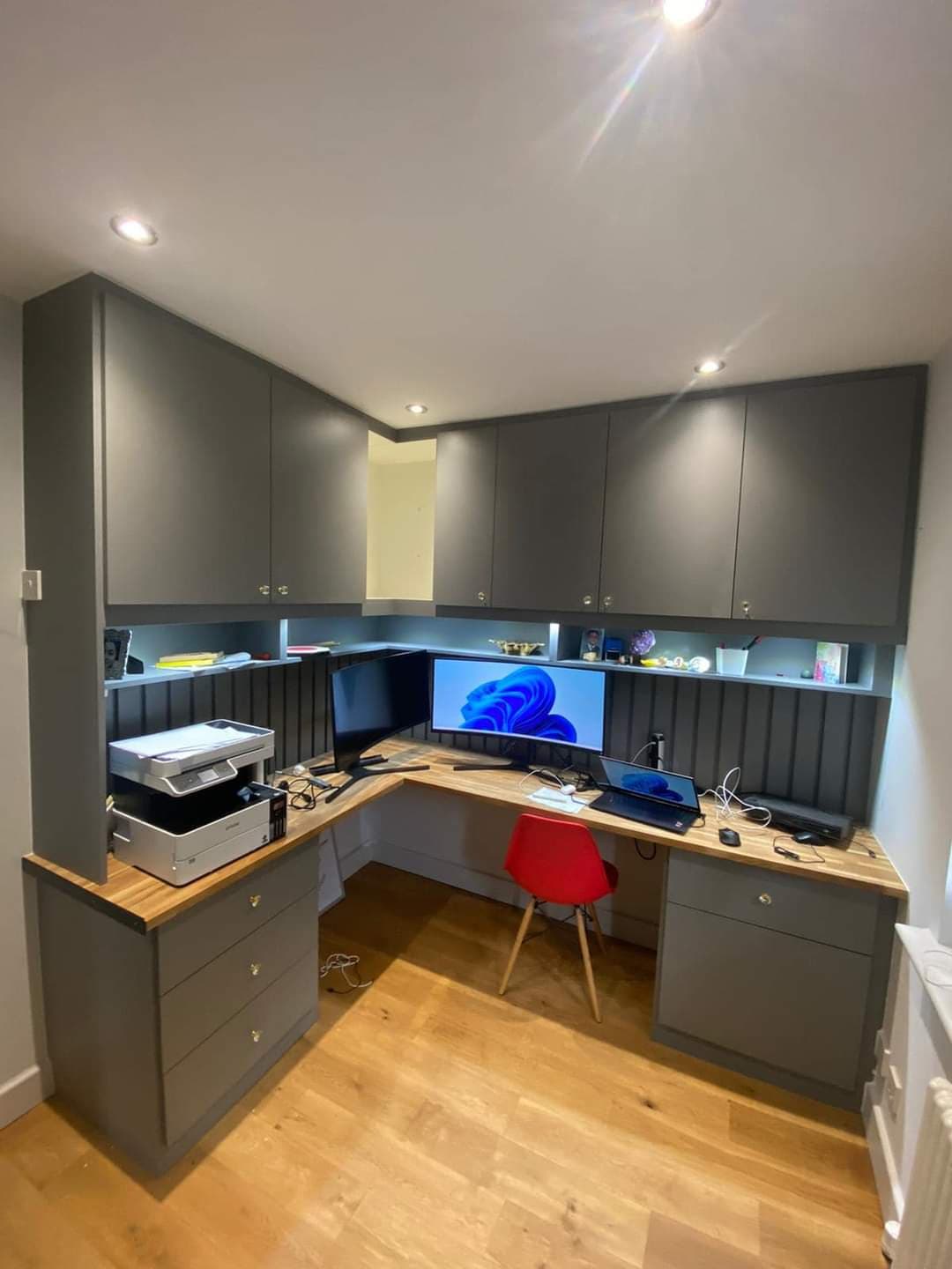 Bespoke L-shaped home office cabinetry with grey hinged doors and integrated wall units.