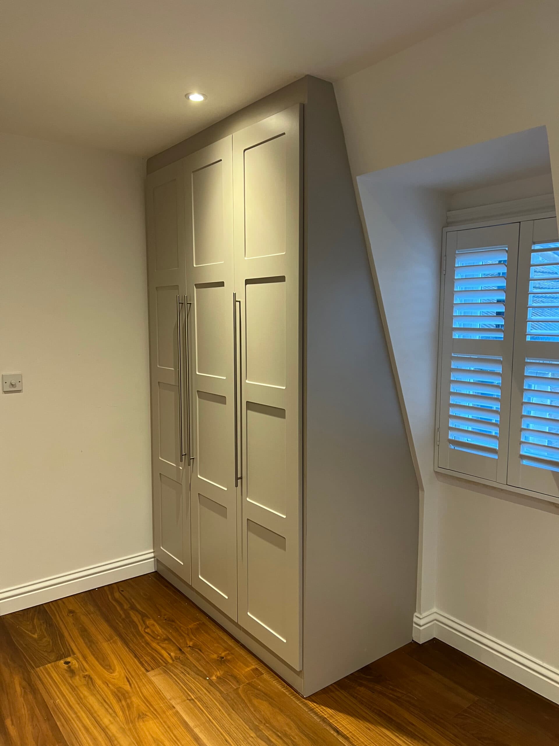 Shaker style fitted wardrobe built under a sloped ceiling with full-length handles.