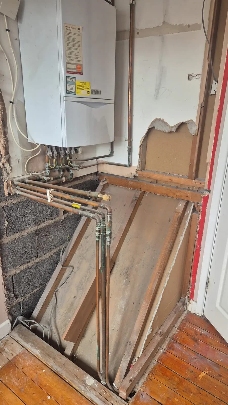 Before: bedroom corner with a wall-mounted boiler, exposed copper pipework and a boxed-in sloping void