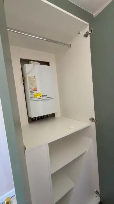 Open wardrobe door showing a boiler housed inside a fitted unit with shelving and a hanging rail