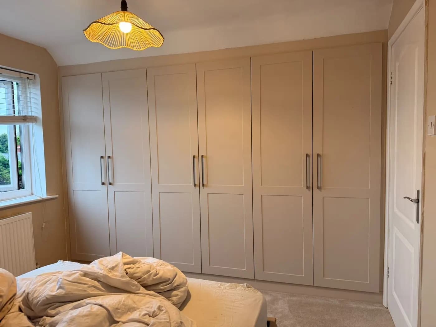 Cream shaker wardrobe doors with long bar handles beside a bedroom window