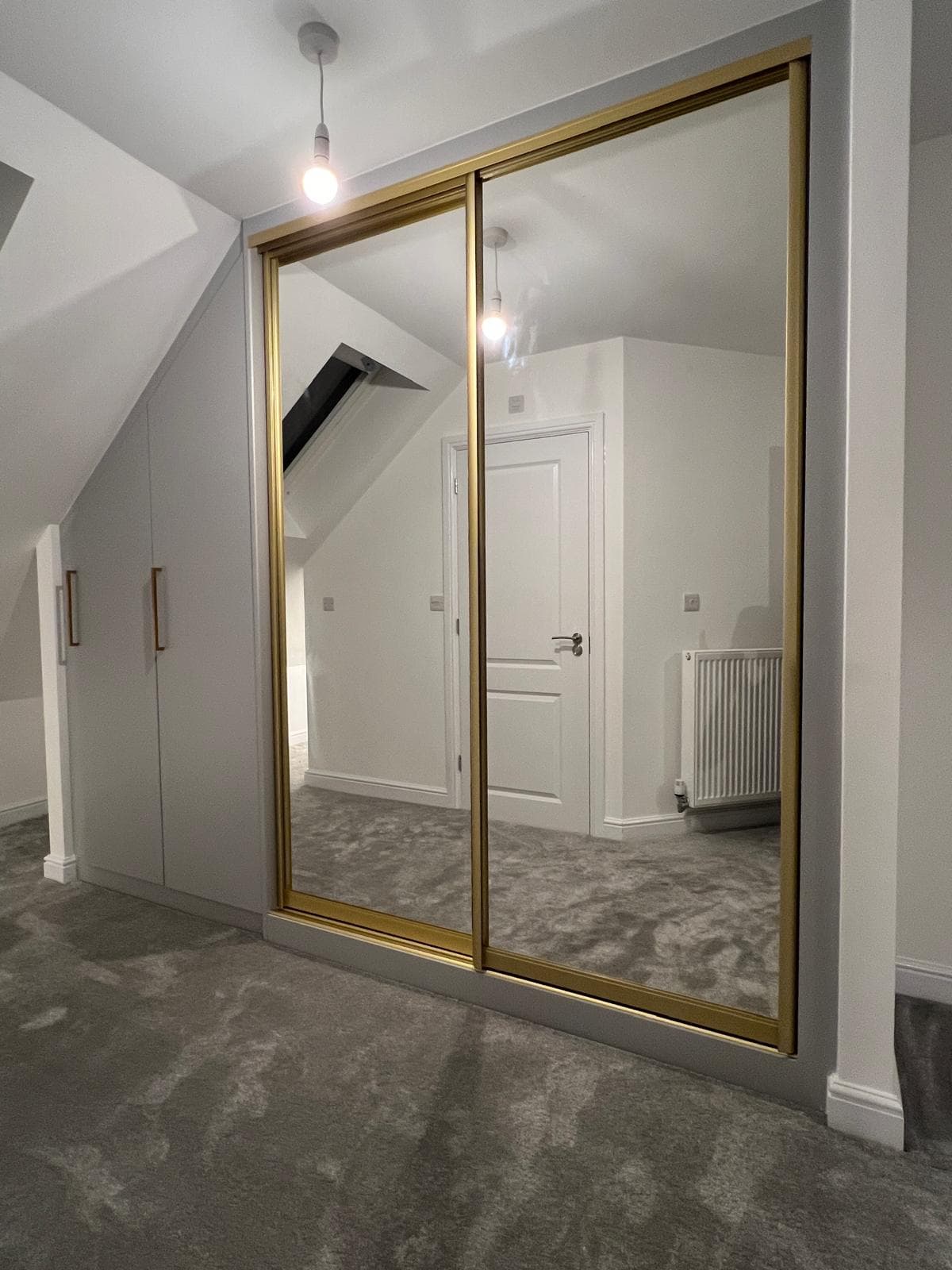 Loft sliding wardrobe built to follow a sloped ceiling, with gold trim detailing.