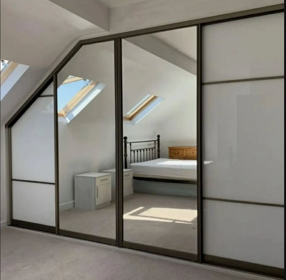 Modern loft wardrobes with mirrored sliding doors and built-in LED lighting fitted into a sloped attic bedroom for stylish storage.
