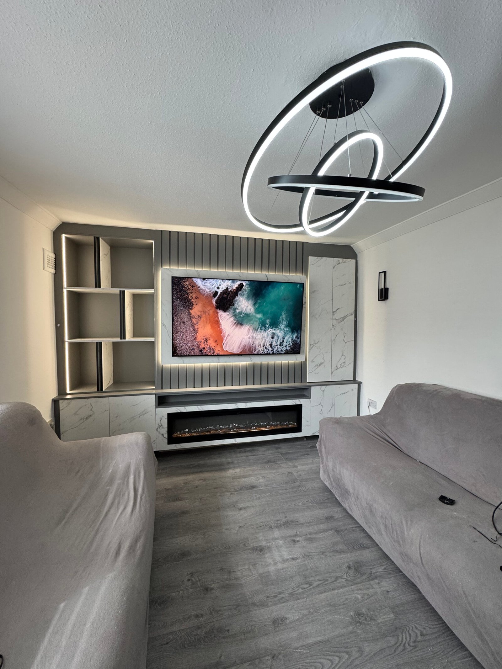 TV screen showing a crashing ocean wave viewed from above, set within a sleek media wall unit accented by soft LED lighting
