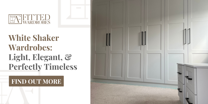 Wall-to-wall white shaker fitted wardrobes with recessed panel doors and vertical black bar handles, installed in a modern bedroom with a neutral carpet and matching chest of drawers