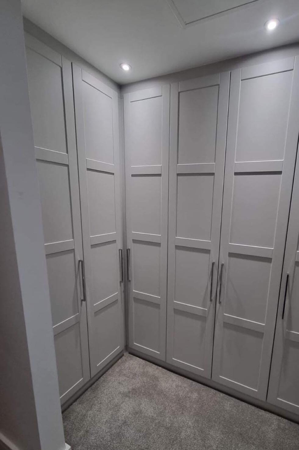 Custom-built corner wardrobe in shaker style with matte grey doors, tall chrome handles, and integrated spotlights.