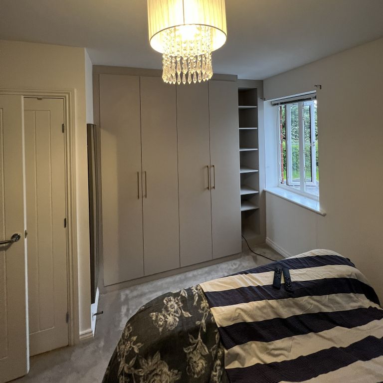 A bright bedroom with fitted wardrobes featuring opening doors, combining timeless design with practical storage solutions.