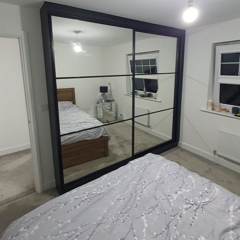 A modern bedroom with sliding glass wardrobes, reflecting elegance and maximising space with fitted bedroom furniture.