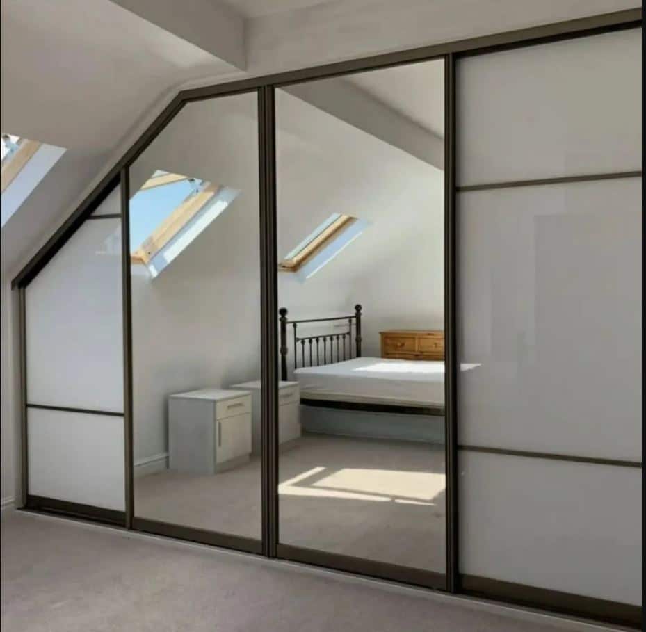 Modern loft wardrobes with mirrored sliding doors and built-in LED lighting fitted into a sloped attic bedroom for stylish storage.