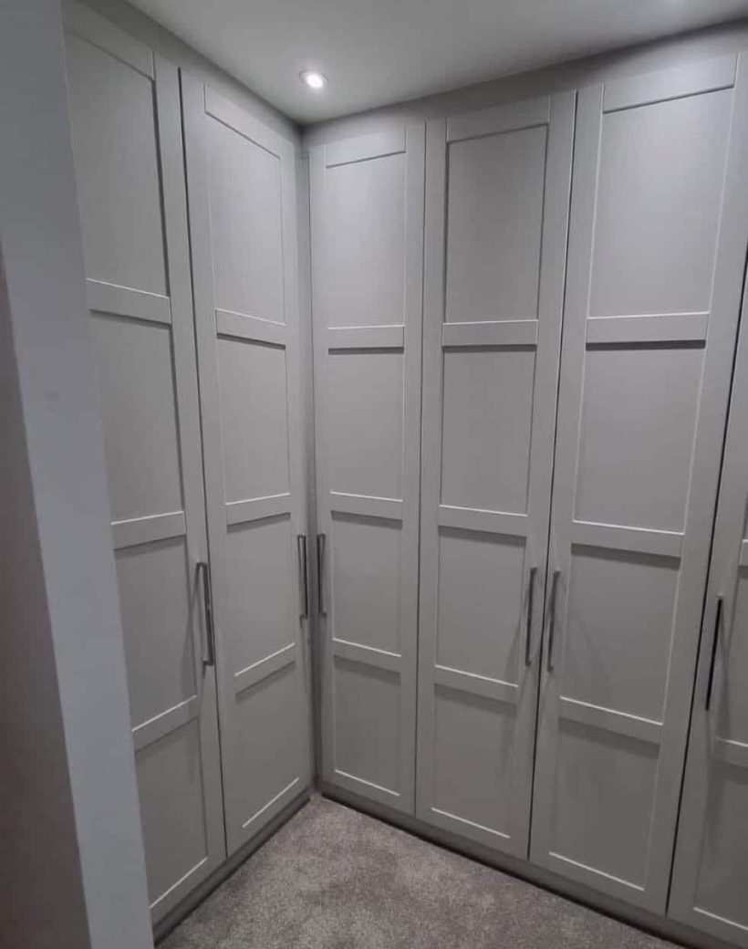 Custom-built corner wardrobe in shaker style with matte grey doors, tall chrome handles, and integrated spotlights.