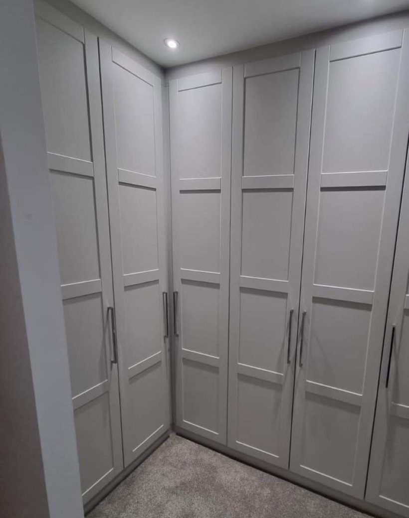 Custom-built corner wardrobe in shaker style with matte grey doors, tall chrome handles, and integrated spotlights.