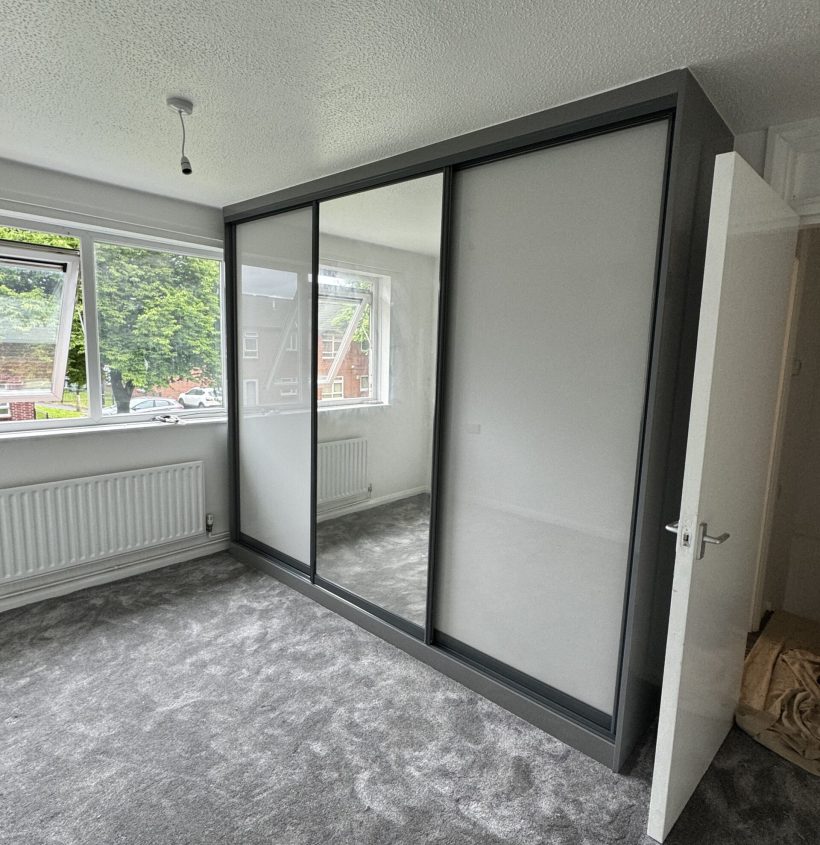 Fitted sliding wardrobe with mirrored panels designed for a compact bedroom.