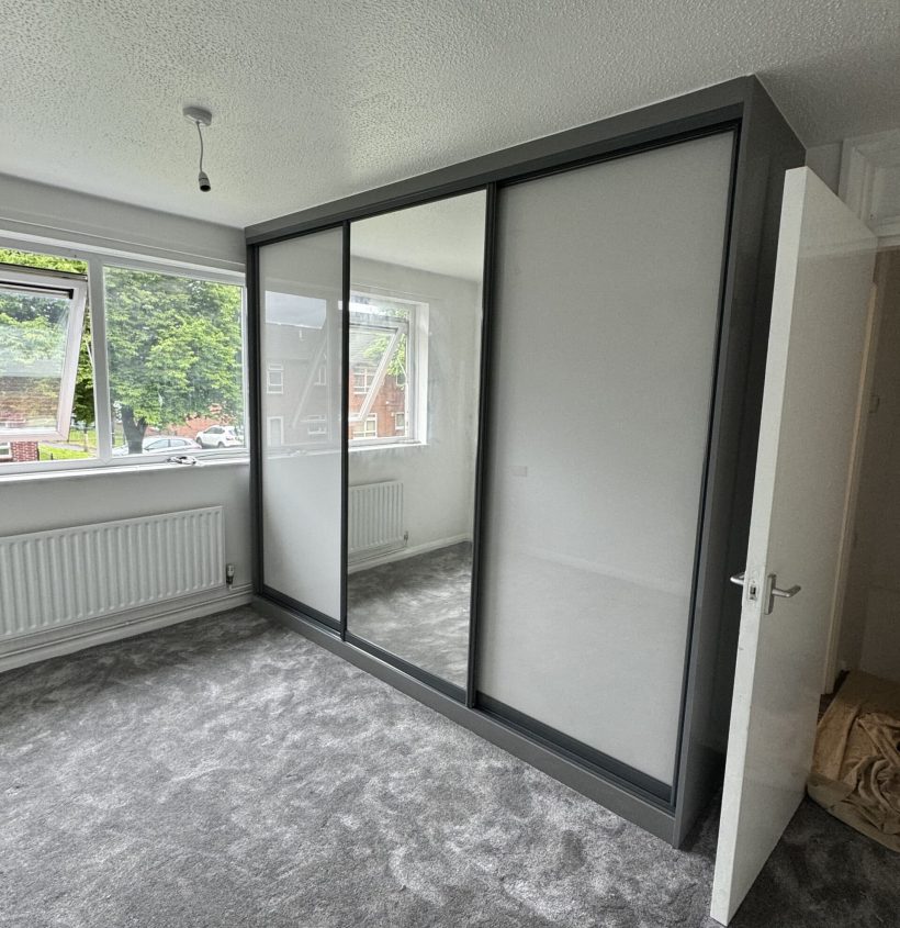 Fitted sliding wardrobe with mirrored panels designed for a compact bedroom.