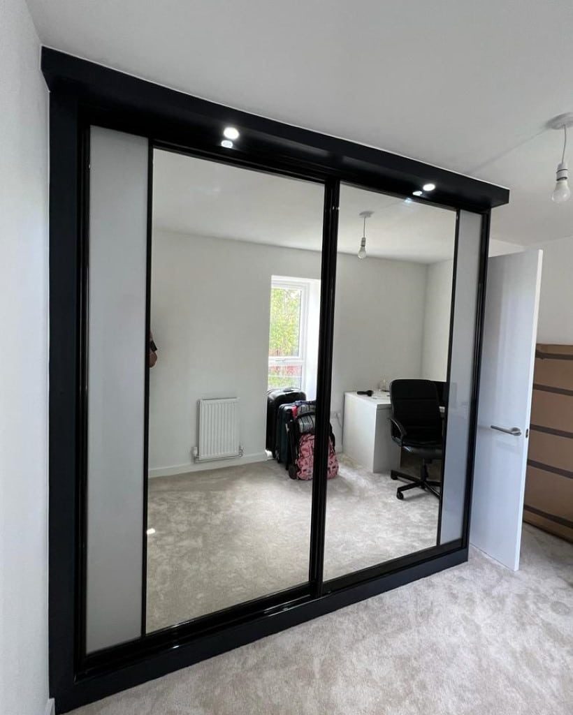 Bespoke sliding wardrobe with black frame and mirrored doors, fitted wall-to-wall in a modern bedroom and home office.