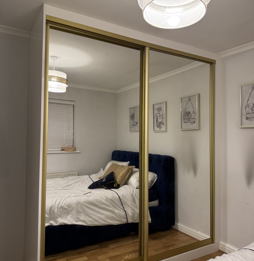 Made to measure sliding wardrobe with gold-trimmed mirrored doors in a modern bedroom.