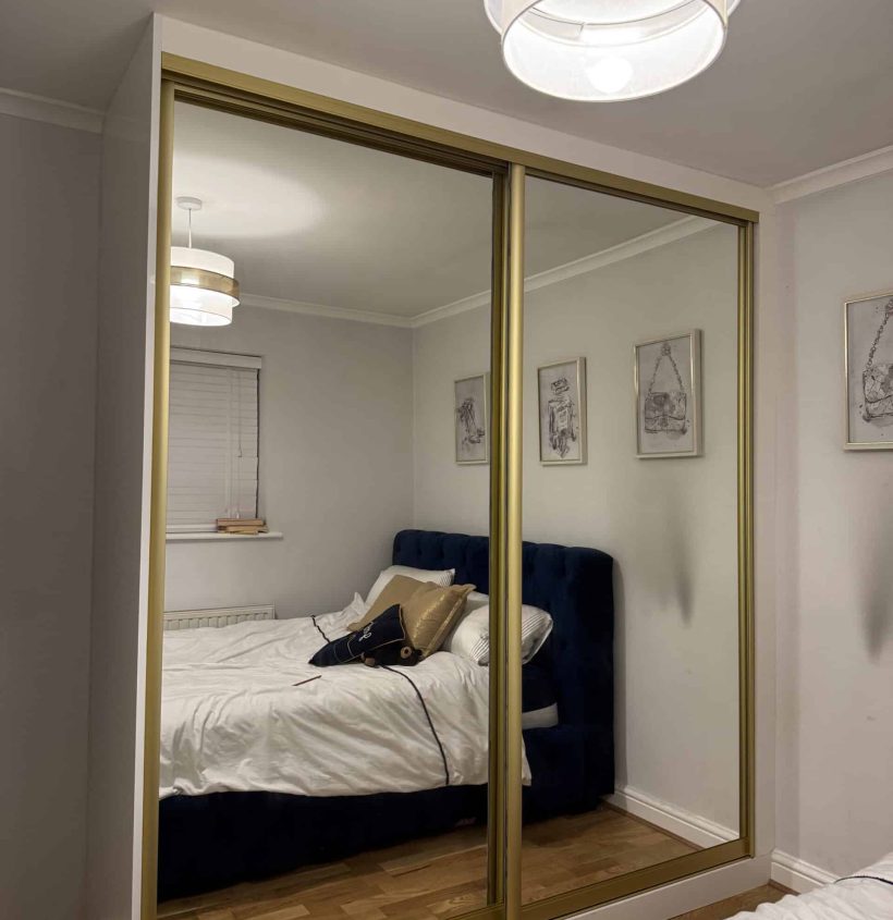 Made to measure sliding wardrobe with gold-trimmed mirrored doors in a modern bedroom.