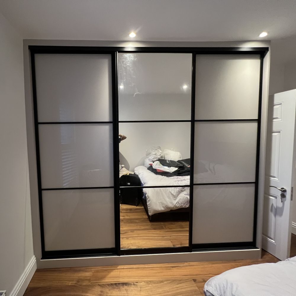 Made to measure wardrobe with sliding doors combining dark wood and mirrored panels.