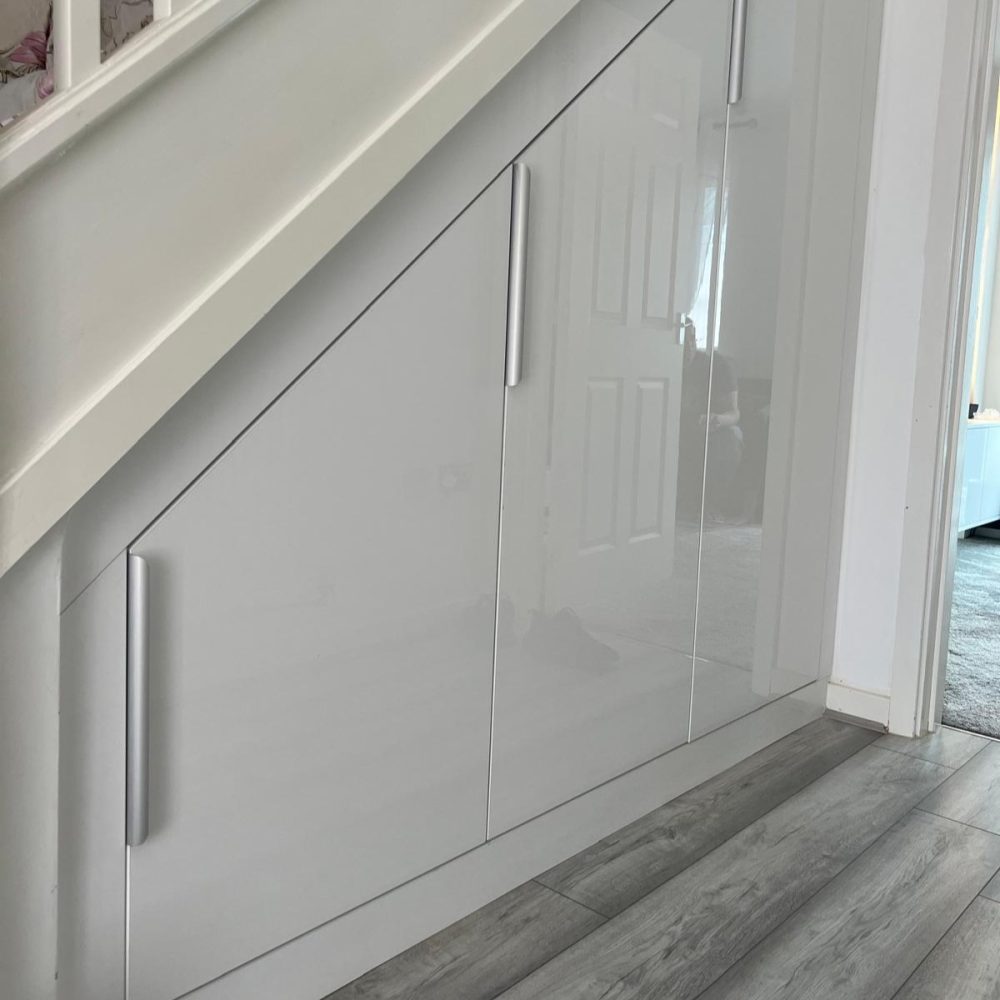 White gloss fitted wardrobe furniture built into under-stairs space with hinged doors
